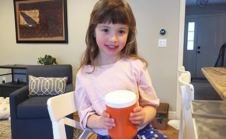 A girl holding a homemade rhythm instrument.