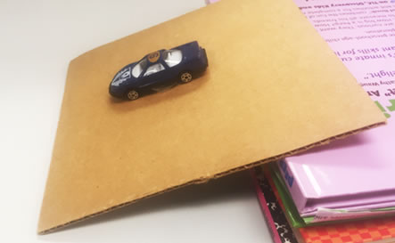 A toy car rolling down cardboard ramp.